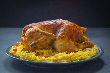 Kabsa - uzun tahıllı basmati pilavından yapılmış Arap yemeği, tam tavuk, soğan, baharatlar: kakule, safran, tarçın, defne yaprakları. Badem ve kuru üzümle süslenmiş. Suudi Arabistan yemeği. Koyu arkaplan.