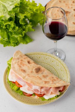 İtalyan piadina romagnola prosciutto, mozzarella peyniri, domates ve salata. Kırmızı şarap kadehi. Üst görünüm.