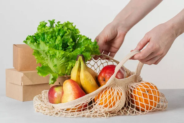 Woman hands with eco string cotton shopper bag with fruits and salad and eco paper boxes. Eco shopping. Reusable, eco friendly concept. Caring for the environment and the rejection of plastic concept.