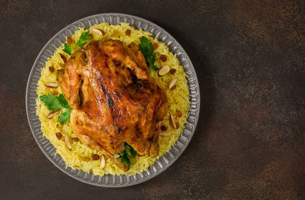 Kabsa - uzun tahıllı basmati pilavından yapılmış Arap yemeği, tam tavuk, soğan, baharatlar: kakule, safran, tarçın, defne yaprakları. Badem ve kuru üzümle süslenmiş. Suudi Arabistan yemeği. Koyu kahverengi arka plan. Üst görünüm.
