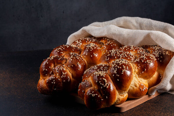 Homemade Challah bread with white cover, Jewish cuisine. Main ingredients are eggs, white flour, water, sugar, salt and yeast. Decorated with sesame and poppy seeds. Dark background.