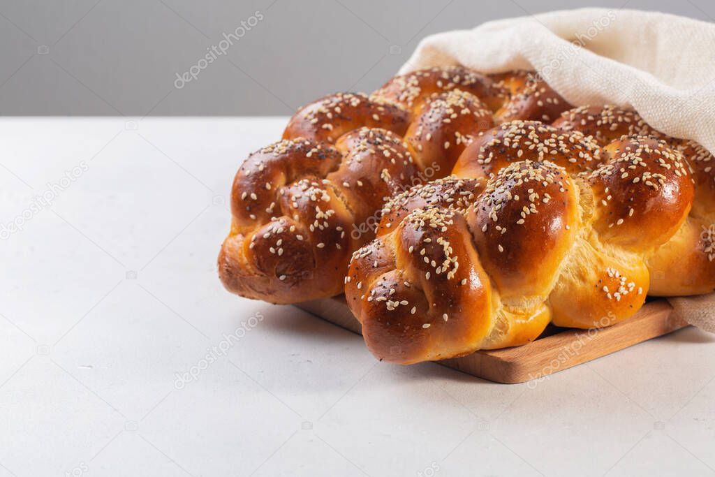 Homemade Challah with white cover - special bread in Jewish cuisine.Main ingredients are eggs, white flour, water, sugar, salt and yeast. Decorated with sesame and poppy seeds. On white table. Copy space.