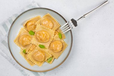 İtalyan yemeği: Kabak ve parmesan peyniri ile doldurulmuş, fesleğenli ve çatallı hafif peçeteyle süslenmiş tortelli ya da ravioli. Beyaz arka plan. Boşluğu kopyala.