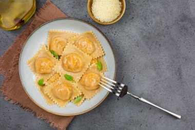 İtalyan yemeği: balkabağı ve parmesan peyniri ile doldurulmuş tortelli ya da ravioli, fesleğenle süslenmiş, çatalla süslenmiş, kahverengi peçeteyle. Gri arka plan. Boşluğu kopyala.
