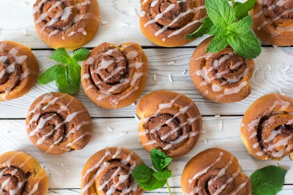 Tarçınlı çörekler ahşap beyaz arka planda, nane ve tarçın çubuklarıyla..