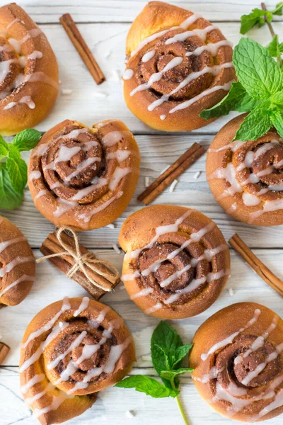 Tarçınlı çörekler ahşap beyaz arka planda, naneli ve tarçınlı çubuklarla. Dikey resim.