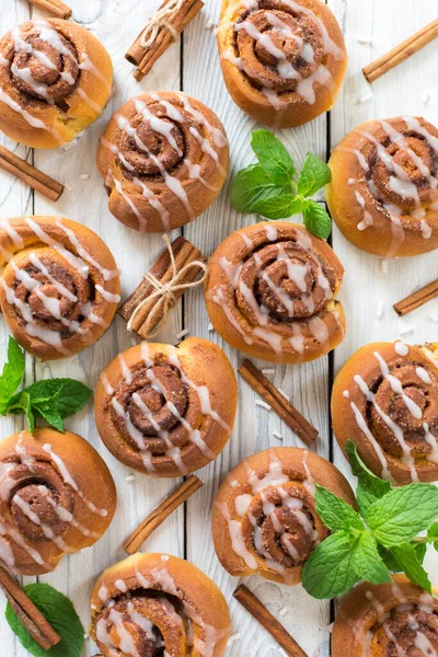 Tarçın çubukları ve taze naneli ahşap beyaz arka planda ev yapımı tarçınlı çörekler. Dikey resim.