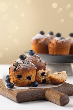 Yaban mersinli çörekler taze yaban mersinli pudra şekerli, muffin bardaksız, beyaz masada, seçici odaklı. Uzayı kopyala Dikey resim.