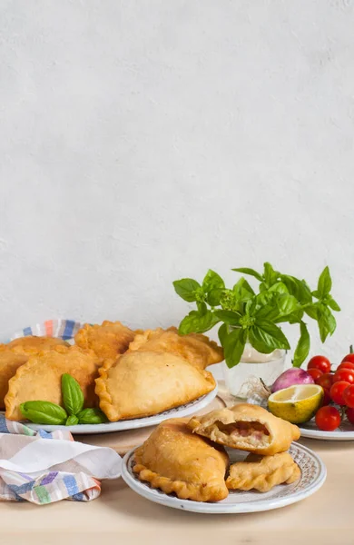 Italian lunch: panzerotti - southern italian fried turnover and vegetables. Turnovers stuffed with mozzarella and mortadella filling. Cotton napkin. Light background, copy space.