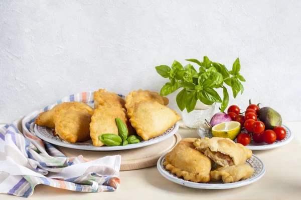 Italian lunch: panzerotti - southern italian fried turnover and vegetables. Turnovers stuffed with mozzarella and mortadella filling. Cotton napkin on light table. Light background, copy space. Copy space.