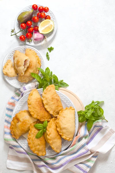 Italian lunch: panzerotti - southern italian fried turnover and vegetables. Turnovers stuffed with mozzarella and mortadella filling. Cotton napkin. Light background, copy space. Top view. Copy space.