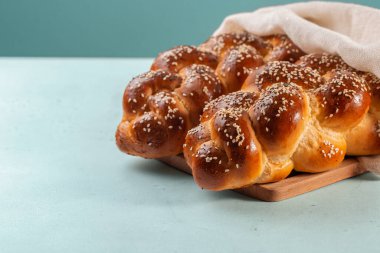 Homemade Challah bread with white cover, Jewish cuisine. Decorated with sesame and poppy seeds. Light green background. clipart
