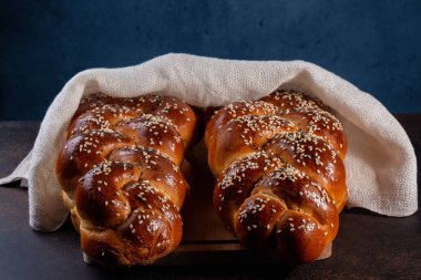Homemade Challah bread with white cover, Jewish cuisine. Decorated with sesame and poppy seeds. Dark background. clipart