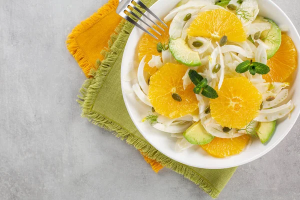 Fresh winter salad: oranges, fennel and avocado with pumpkin seeds. On green and orange napkins. Grey background. Top view. Copy space.
