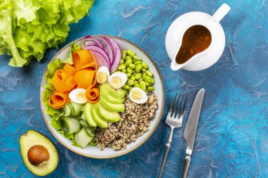 Bıldırcın yumurtalı Buda kasesi, sağlıklı yiyecek konsepti. Kinoa, edamame fasulyesi, avokado, ququmber, havuç, kırmızı soğan ve yeşil salata. Fıstık ezmesi, soya sosu, sarımsak ve zencefilden yapılan sos..