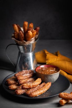 Churros ile bir tabak - kızarmış hamur, dulce de leche, yavaşça tatlandırılmış yoğunlaştırılmış süt. Koyu arkaplan, dikey resim. 