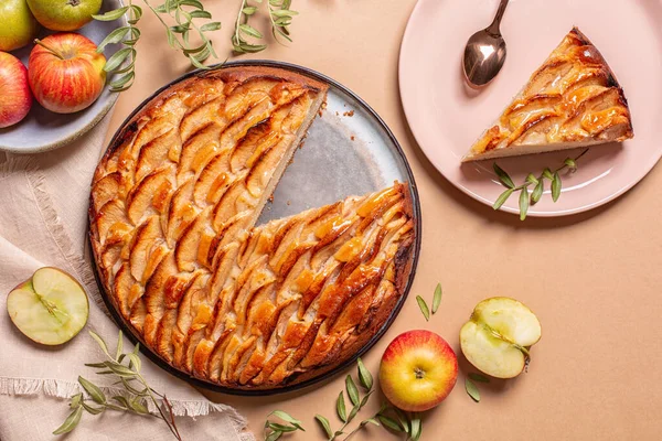 Apple pie and piece of pie decorated with apple slices and glazed. Fresh apple fruits, on a peach background. Copy space.