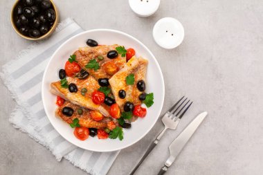 Pişmiş levrek balığı filetosu, İtalyan usulü balık güveci, siyah zeytin, domates ve kapari, taze maydanozlu. Açık gri arka planda. Üst görünüm.