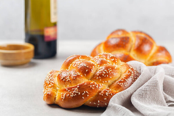 Homemade challah bread rolled into circular shape with a cover, contains eggs, olive oil, water, yeast, topped with sesame. Wine  and salt are in background.