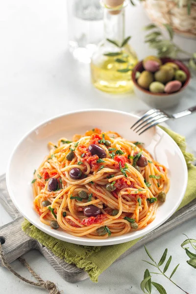 İtalyan yemeği. Spagetti alla puttanesca - domatesli İtalyan makarna tabağı, zeytin, kapari ve maydanoz. Hafif arkaplan. Uzayı kopyala Dikey resim.