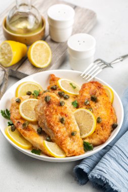 Chicken piccata on white table. Chicken breast dredged in flour and cooked in sauce cantaining lemon juice, butter and capers. Close-up. Vertical image. clipart