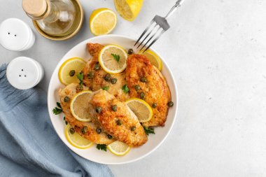 Chicken piccata on white table directly above. Chicken breast dredged in flour and cooked in sauce cantaining lemon juice, butter and capers.  clipart