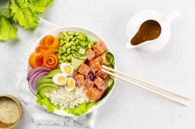 Somon balığı, pilav, avokado, kırmızı soğan, salatalık, edamame fasulyesi, havuç ve bıldırcın yumurtası, susamlı deniz ürünleri. Soya sosu, fıstık ezmesi, sarımsak ve zencefilden yapılmış sos. Beyaz arkaplan. 