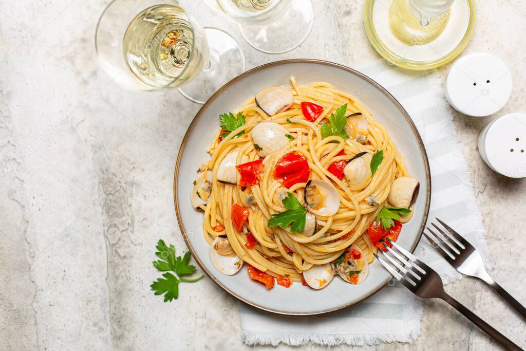 Italian dinner, seafood pasta and white wine. Spaghetti alle vongole or clams, tomato and parsley. Light stone background.