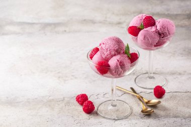 Strawberry ice cream with fresh raspberries in a glass bowl on a stone surface. Two portions. Copy space.