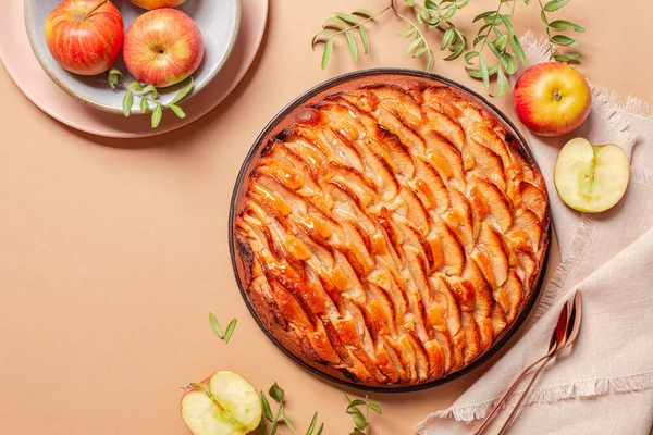 Apple pie decorated with apple slices and glazed. Fresh apple fruits, on a peach background. Copy space.