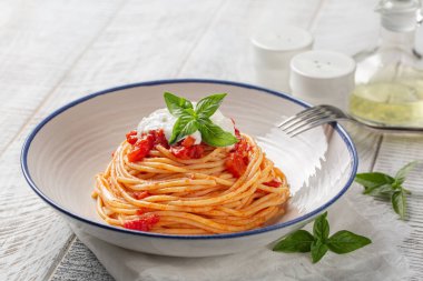 Klasik İtalyan makarnası domates soslu, stracciatella peynirli ve fesleğen yapraklı. Beyaz ahşap masada..