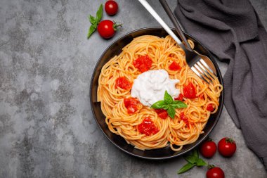 Stracciatella ile spagetti ve domatesler koyu gri arka planda siyah tabakta.