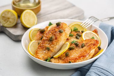 Chicken breast dredged in flour and cooked in sauce cantaining lemon juice, butter and capers. Chicken piccata. White table. clipart