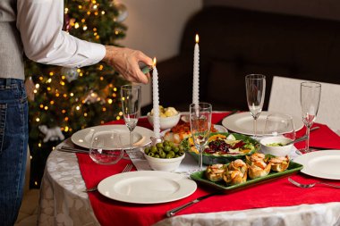 Adam Noel 'de, yeni yıl masasında mum yakıyor. Ev yapımı yemek, kanepe, karides ve guacamole turtası, kış salatası, zeytin, yunan balığı, bardak. Akşam yemeği partisinin yaşam tarzı foto.