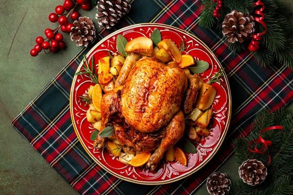 Noel veya Yeni Yıl ziyafeti manzarası, elma ve portakalla doldurulmuş kızarmış tavuk ve fırında patates, adaçayı ve biberiye ile birlikte yeşil ve kırmızı bir tartan peçetesi üzerinde servis edilen güzel bir kırmızı tabak.. 