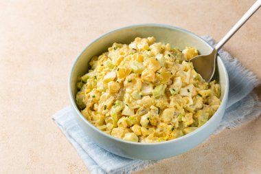 Bej arka planda patates salatası ve açık mavi kasenin yüksek melek manzarası. Haşlanmış patates, haşlanmış yumurta, soğan, kereviz, hardal, turşu, mayonez ve kırmızı biber sosundan yapılmış. Arkaplandaki İçindekiler.