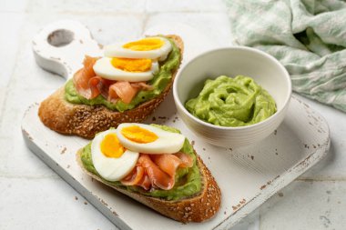 İki füme somon tostlu beyaz tahta ve kremalı Avokado. Susamlı ekmek, haşlanmış yumurta. Ev yapımı açık sandviçi kapat. Sağlıklı kahvaltı..
