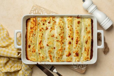 Fırınlanmış Cannelloni, ıspanak ve ricotta ile doldurulmuş yumurta bazlı makarna, İtalyan mutfağında peynir ve beşamel sosuyla kaplanmış. Bej tablo.