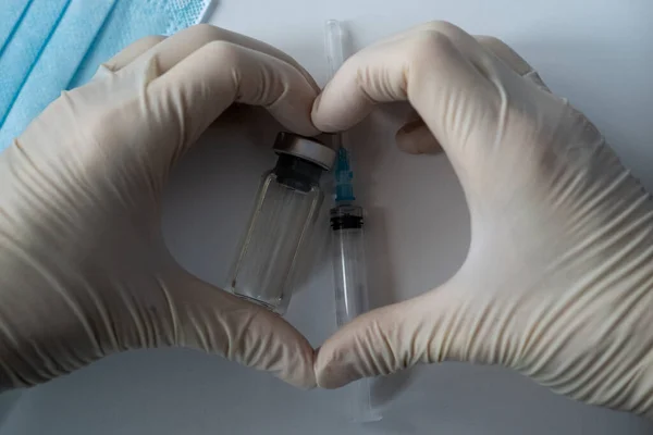 Enfeksiyon aşısı, şırınga ve koruyucu maskeli şişeler. Elleri koruyucu eldivenlerde kalp.