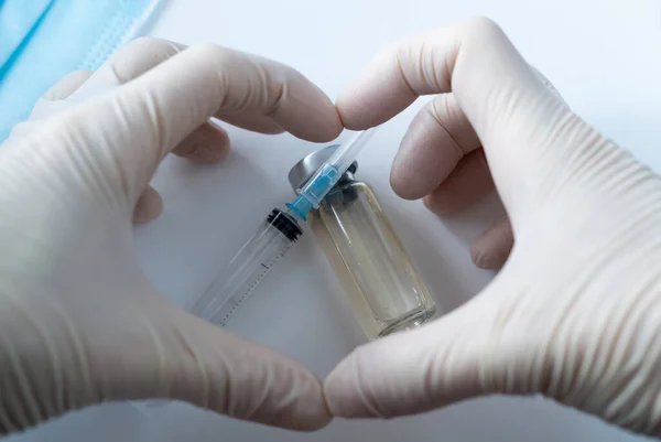 Enfeksiyon aşısı, şırınga ve koruyucu maskeli şişeler. Elleri koruyucu eldivenlerde kalp.