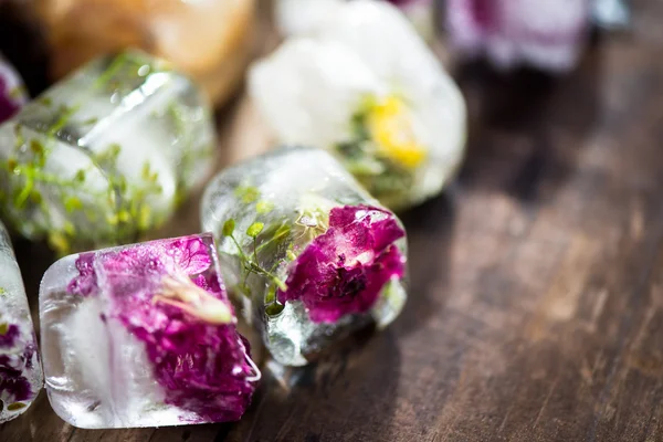 Gefrorene Blumen in Eiswürfeln auf rustikalem Holzgrund — Stockfoto