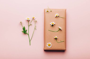 Geri dönüşümlü kahverengi kağıda sarılmış gerçek taze papatyalarla süslenmiş, minimalist stil ambalajlı açık arkaplan, üst görünüm düz yatak, çevre dostu ve sıfır atık ambalajı