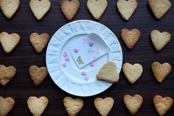 Assiette blanche avec note Je t'aime et biscuits en forme de coeur autour — Photo