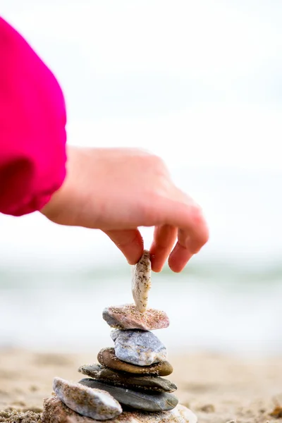 Pequena Mão colocando Pedra na Pirâmide na areia. Mar no bac — Fotografia de Stock