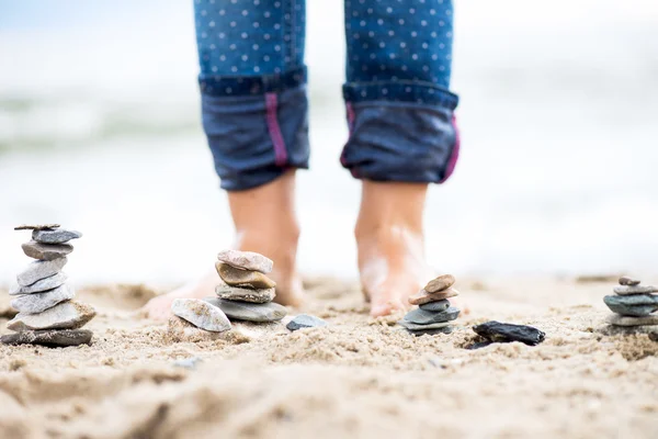 Gyerekek lába és a kövek piramisok a homok. A tenger a háttérben — Stock Fotó