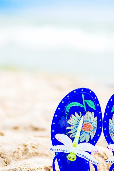 Sandalias de gelatina azul con libélula en la arena. Mar en el —  Fotos de Stock
