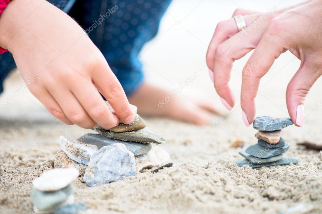 Hands placing Stones on the Stone Pyramids on sand
