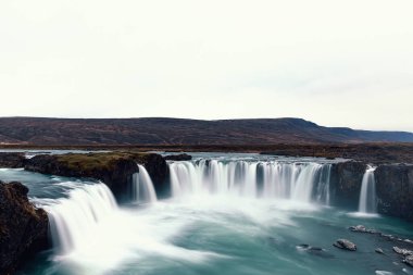 Arka planda dağlar olan Godafoss şelalesinin etkileyici uzun pozlama manzarası. Popüler turizm, İzlanda 'da seyahat yeri.