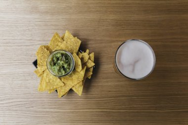 Bir tabak nachos ve guacamole. Yanında da tahta bir barda bira.