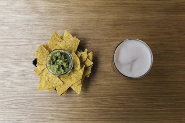 Bir tabak nachos ve guacamole. Yanında da tahta bir barda bira.
